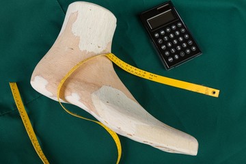 a wooden last on a green clobber with a measuring tape and a calculator