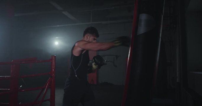 In a large cross fitness class young strong man with a perfect muscle boxing hard and concentrated wearing boxing gloves