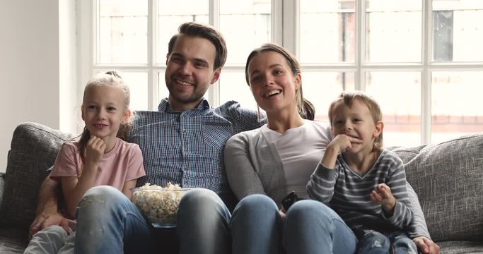 Happy parents and cute little children watching tv at home