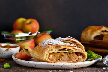 Apple strudel with cinnamon, nuts and and raisins on a dark concrete background.