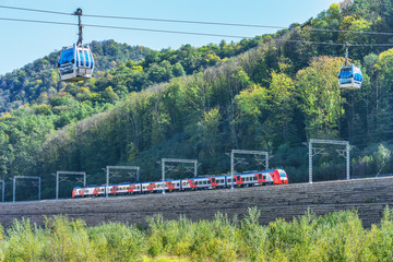 Passenger train from Roza Khutor to Sochi moves under the cableway.. Krasnaya Polyana. Russia.