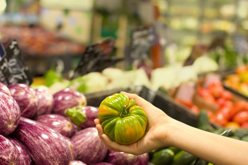Female hand choosing green tomato in supermarket. Concept of healthy food, bio, vegetarian, diet.
