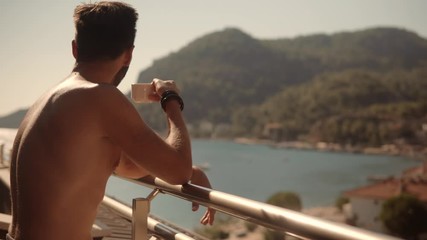 Man Drinking Coffee On Porch And looking At View Sea.Lonely Romantic Man Rest And Looks At Ocean.Attractive Italian Man Stay On Balcony Looking At Calm Sea And Drinking Tea.Guy Relaxing Morning Porch - Powered by Adobe