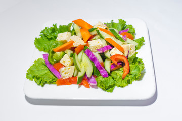Fresh green vegetable salad in a plate. Healthy capsicume, carrot, cheese, tomato and lettuce meal on white background