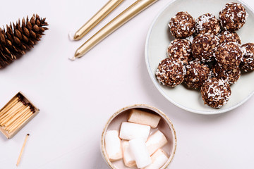 Swedish chocolate balls and cup of cocoa with marshmallow on grey concrete table. Cozy winter breakfast. Chokladbollar. Homemade healthy raw cocoa oatmeal balls sprinkled with coconut flakes