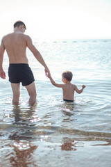 Young father and his little son play together in a water. Scenic sea and mountain view, summer time vacation