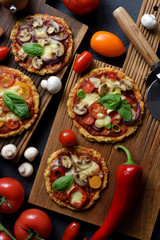 Fototapeta na wymiar Healthy comfort food or keto diet concept. Cauliflower gluten free pizzas with mushrooms, eggplants, tomatoes and basil with raw ingredients on dark background