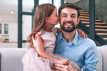 small daughter kissing her dad sitting on the couch in living room