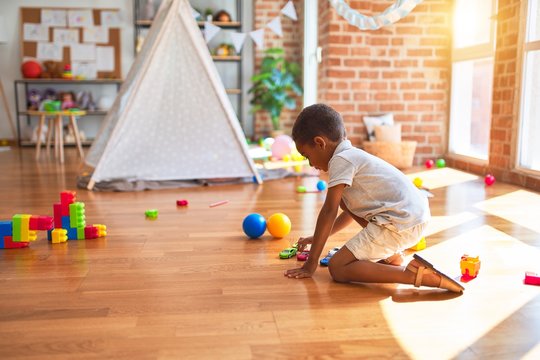 Beautiful african american toddler playing with cars around lots of toys at kindergarten