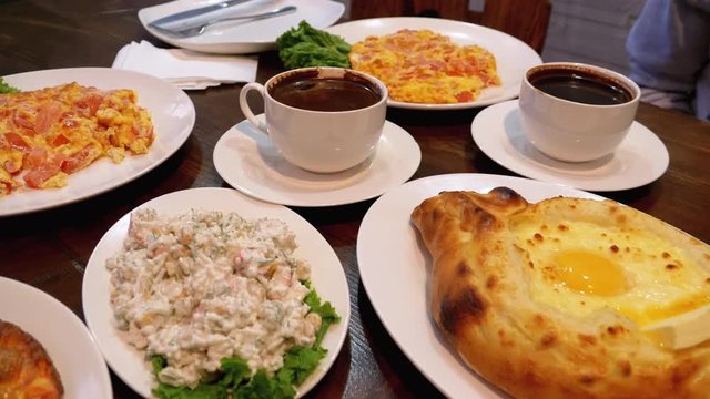 Adjarian Khachapuri on a Table in a Georgian Restaurant next to Salad, Omelette and Coffee