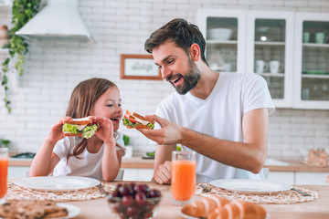 dad feeding girl eating with his sandwich for breakfast on the kitchen