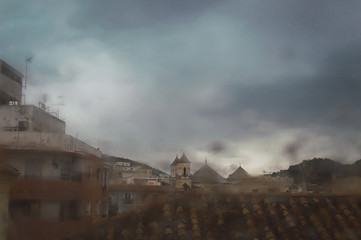 Views of a city and buildings through a window with raindrops during a stormy day of winter.