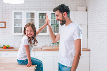 daughter giving high five to her dad sitting on the table on the kitchen