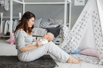 Happy family in gray scandinavian children's room. Little Boy with his mother weared in pajamas. Good morning of Mom and infant son in sleepwear. Family weekdays traditions. Relationship with love