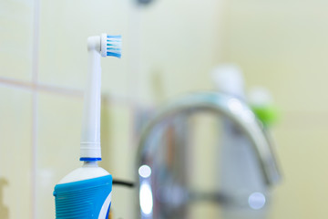 A modern electric toothbrush in white and blue colour stands on the edge of the bathroom sink.
