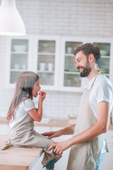 side view of little girl eating cherry tomato with father on the domestic kitchen