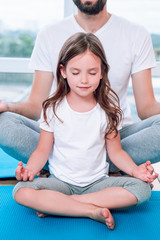 cropped shot of father and daughter sitting in lotus position together at home