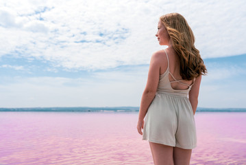 Fototapeta na wymiar Back view of cute teenager woman wearing summer clothes on pink lake