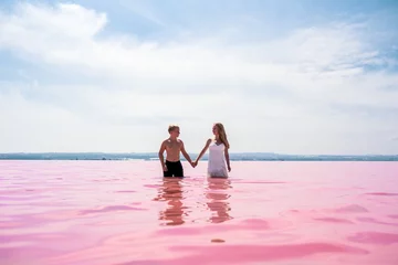 Fototapeten cute teenager couple walking on a shore of amazing pink lake © DavidPrado