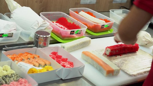 Asian cook master cooking and make rolls. A man in transparent sterile gloves roll in batter and breadcrumbs tasty rolls in kitchen. Sushi rolls with rice and fish prepare for people on sale and eat.
