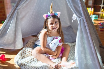 Adorable toddler sitting on the floor inside tipi around lots of toys at kindergarten