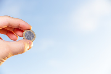 hand holding 1 euro coin over clear blue sky, Exchange money. Financial concepts, Business Concept.