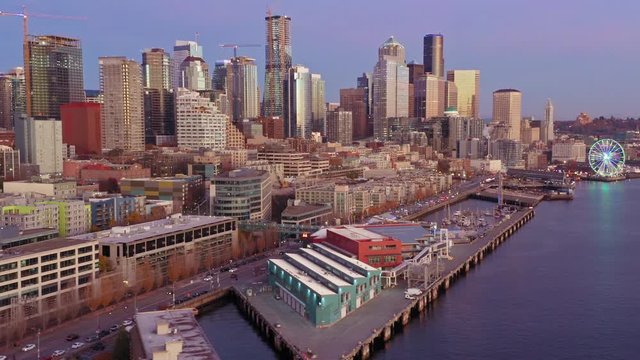 Aerial: Flying over the Seattle city skyline, Alaskan Way and Elliott Bay waterfront at sunset. Washington, USA