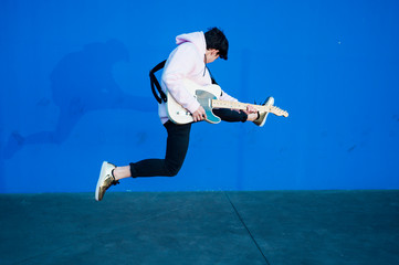 Fototapeta na wymiar young man jumping with electric guitar on blue background