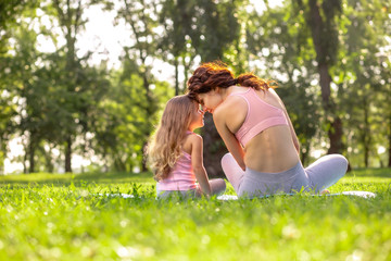 back view of mother and daughter in sport wear sitting on the yoga mat head to head