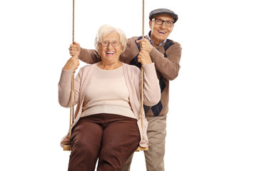 Elderly man pushing an elderly woman on a swing