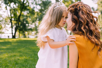 portrait of mother kissing her daughter in the park, side view