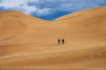 Fototapeta na wymiar Two travelers in the desert. Hiking on sand dunes in mountains. Gobi desert, Mongolia