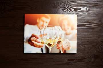 Canvas photo print on brown wooden background. Stretched foto with wine glasses and people . Front view of colorful photography hanging on a wall