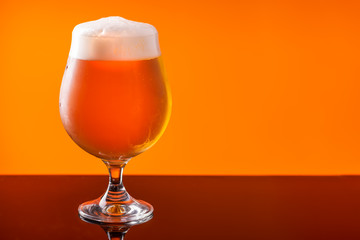 Beer glass with drops on a orange background. Alcohol concept. Copy space
