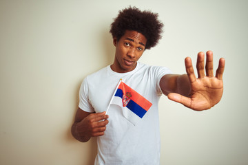 Young afro american man holding Serbia Serbian flag standing over isolated white background with...