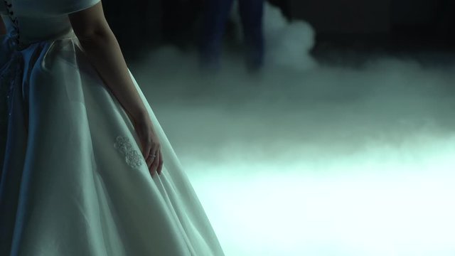 Handsome woman hold beautiful luxury white dress and stands in puffs of fluffy fog on the floor close up. Loving couple in happy married day. Bride and groom are preparing for first wedding dance. 