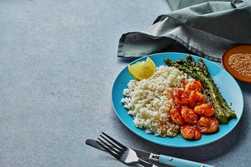 Plate of chili shrimps stir fry, grilled asparagus and basmati rice on a blue stone table. Gourmet seafood meal shot with free space for you text.