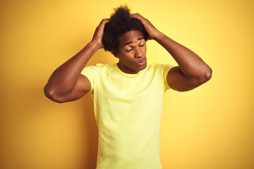 Fototapeta na wymiar African american man with afro hair wearing t-shirt standing over isolated yellow background suffering from headache desperate and stressed because pain and migraine. Hands on head.