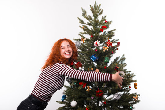 Image of Happy young woman embrace christmas tree while standing over white background
