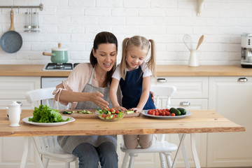 Smiling young woman giving first culinary class to daughter.