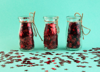 Glass jars with red glitter confetti of various shapes on minty background. Holiday Christmas and New Year background.