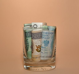 Rolls of banknotes of 200 and 100 Polish zloty into glass close up isolated on pastel peach background