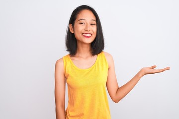 Young chinese woman wearing yellow casual t-shirt standing over isolated white background smiling cheerful presenting and pointing with palm of hand looking at the camera.