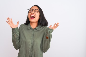 Young chinese woman wearing green shirt and glasses over isolated white background celebrating crazy and amazed for success with arms raised and open eyes screaming excited. Winner concept