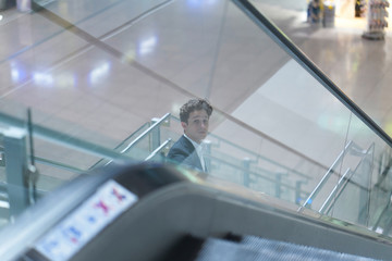 Young attractive businessman going down on an escalator in the airport, looking up