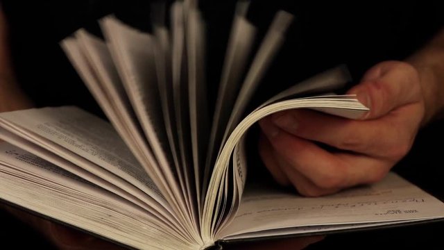 a man leafs through a book with a black background at the back