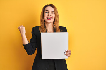 Young redhead businesswoman with clear eyes holding banner over isolated yellow background screaming proud and celebrating victory and success very excited, cheering emotion