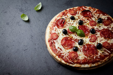 Pizza with chorizo, mozzarella cheese, cherry tomatoes, black olives and oregano. Home made food. Concept for a tasty and hearty meal. Dart stone background. Close up. Copy space.