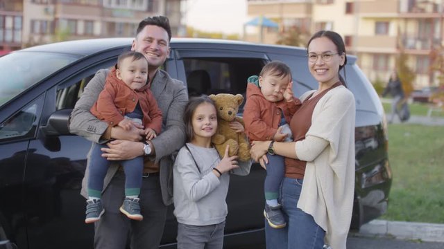 Portrait Of Happy Family With Children Standing In Front Of Parked Car And Looking At Camera