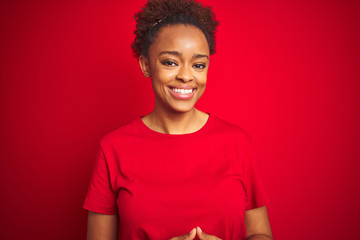 Young beautiful african american woman with afro hair over isolated red background with hands together and crossed fingers smiling relaxed and cheerful. Success and optimistic